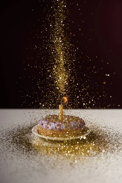 Палаюча свічка посеред пончика з падаючими золотими блискітками ізольовані на чорному — стокове фото