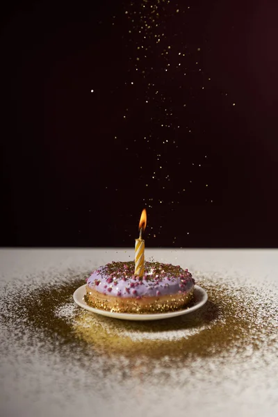 Vela ardente no meio de donut saboroso com brilho caindo isolado em preto — Fotografia de Stock