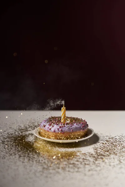 Candle in middle of doughnut with golden sparkles on white table isolated on black — Stock Photo