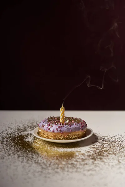 Candle in middle of tasty doughnut with shiny sparkles on white table isolated on black — Stock Photo