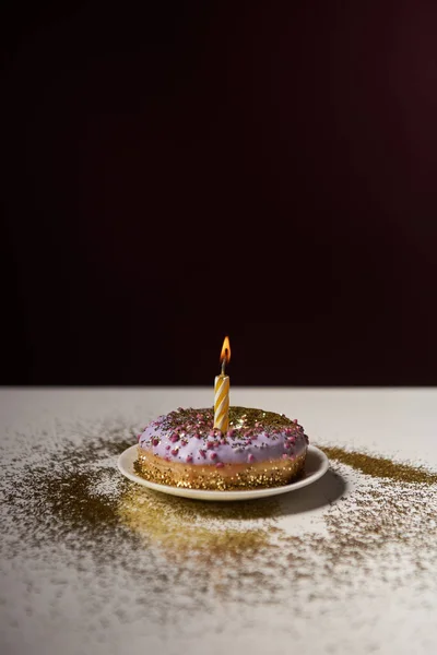 Candle in middle of sweet donut with shiny sparkles on white table isolated on black — Stock Photo