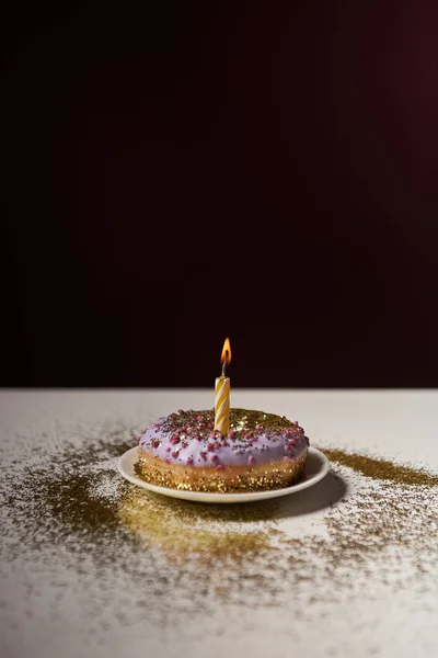 Vela en medio de una rosquilla dulce con destellos brillantes sobre una mesa blanca aislada en negro - foto de stock