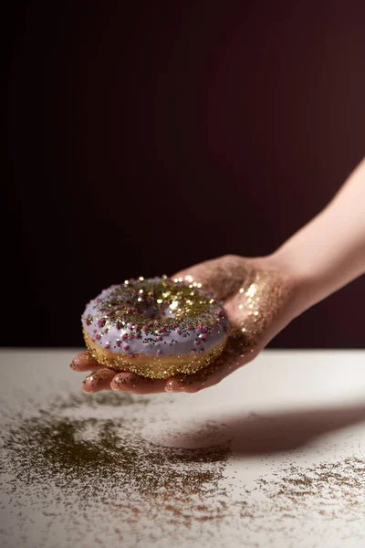 Vista cortada de mulher segurando donut com brilhos dourados na mão isolado em preto — Fotografia de Stock