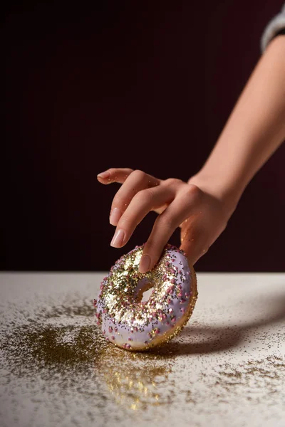 Vista cortada de mulher segurando donut com brilhos brilhantes na mão isolado em preto — Fotografia de Stock