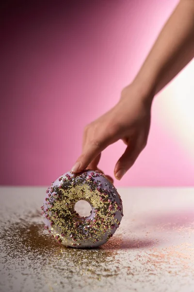 Cropped view of woman holding sweet doughnut with golden sparkles on pink background — Stock Photo