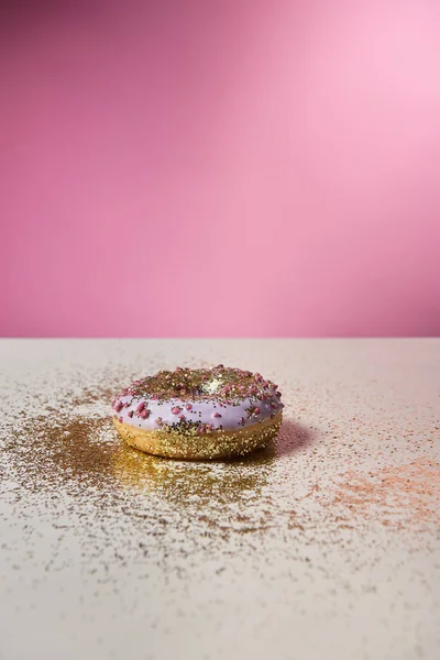 Beignet glacé avec des étincelles brillantes sur table blanche sur fond rose — Photo de stock