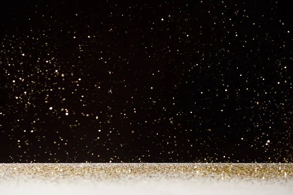 Selective focus of golden sparkles falling on white table isolated on black — Stock Photo