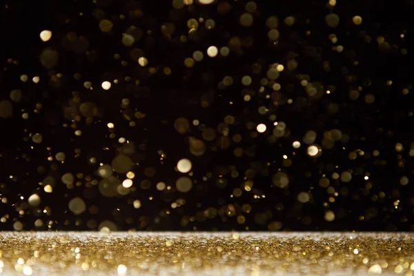 Selective focus of bright sparkles falling on table isolated on black — Stock Photo