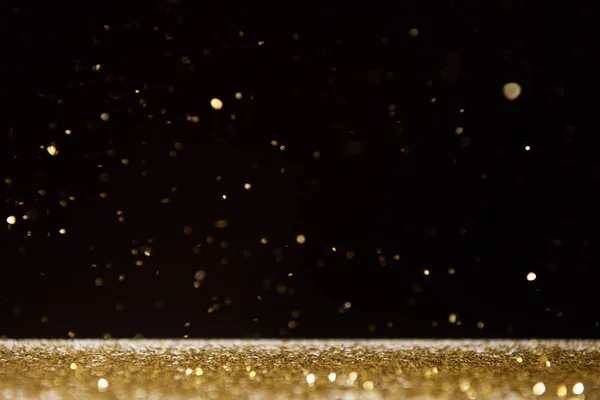 Selective focus of golden sparkles falling on table isolated on black — Stock Photo