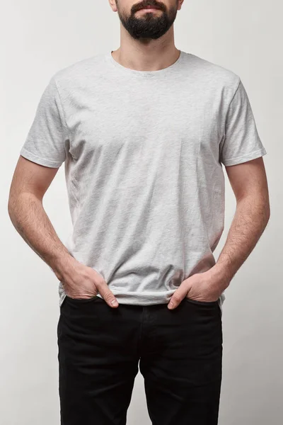 Vista cortada de homem barbudo com as mãos em bolsos em t-shirt branca com espaço de cópia isolado em cinza — Fotografia de Stock