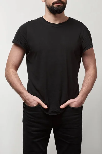 Visão parcial do homem com as mãos nos bolsos em t-shirt preta com espaço de cópia isolado em cinza — Fotografia de Stock