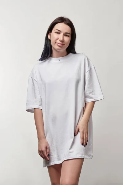 Belle jeune femme en t-shirt oversize blanc avec espace de copie regardant la caméra isolée sur gris — Photo de stock