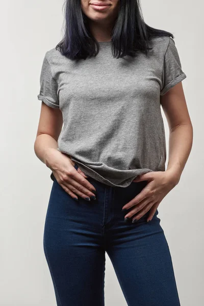 Обрезанный вид молодой женщины в джинсах и серой футболке с копировальным пространством, изолированным на белом — стоковое фото