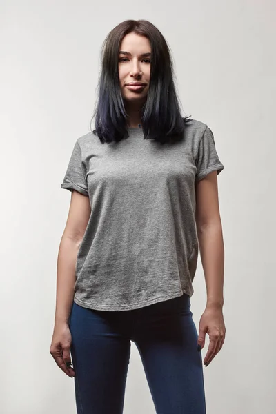 Hermosa mujer joven en camiseta gris con espacio de copia mirando a la cámara aislada en blanco - foto de stock