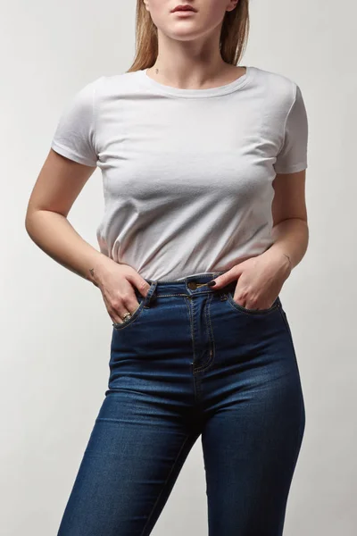 Visión parcial de la joven en mezclilla y camiseta blanca con espacio de copia aislado en gris - foto de stock
