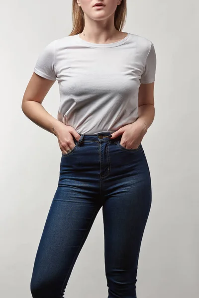 Visión parcial de la joven en mezclilla y camiseta blanca con espacio de copia aislado en gris - foto de stock