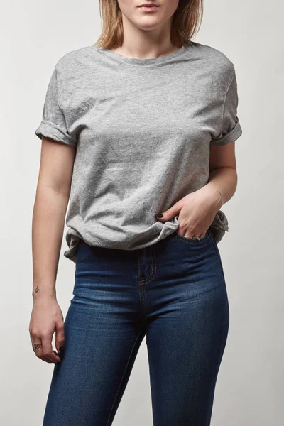 Vue recadrée de jeune femme avec la main dans la poche en t-shirt gris avec espace de copie isolé sur blanc — Photo de stock