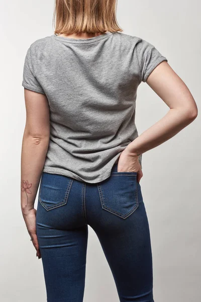 Vista trasera de mujer joven en camiseta gris casual con espacio de copia aislado en blanco - foto de stock