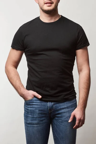 Partial view of man with hand in pocket in denim and black t-shirt with copy space isolated on grey — Stock Photo