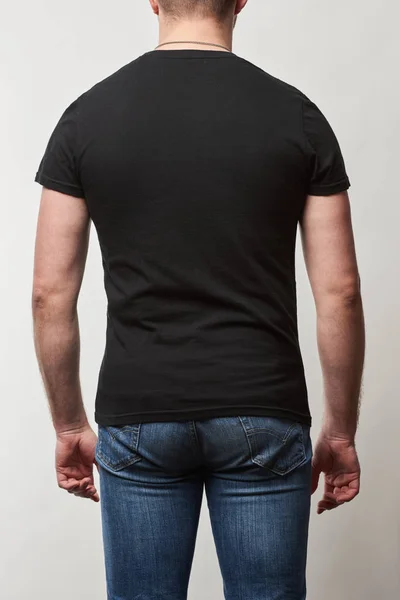 Vista trasera del hombre en mezclilla y camiseta negra con espacio de copia aislado en gris - foto de stock