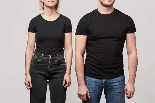 Обрізаний вид молодого чоловіка і жінки в чорних футболках з копіювальним простором ізольовано на сірому — Stock Photo