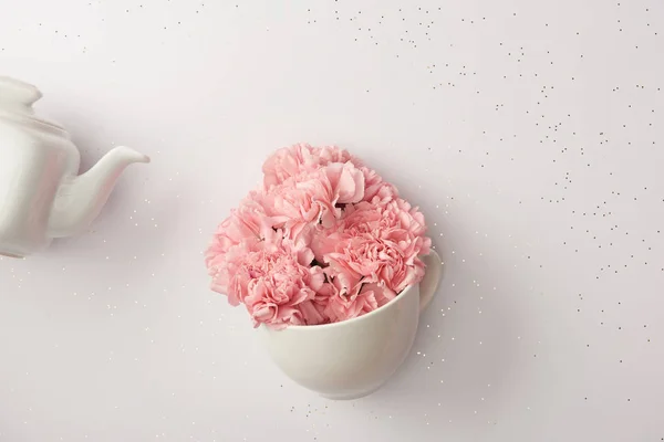 Рожеві квіти гвоздик в чашці і білий чайник ізольовані на сірому — стокове фото