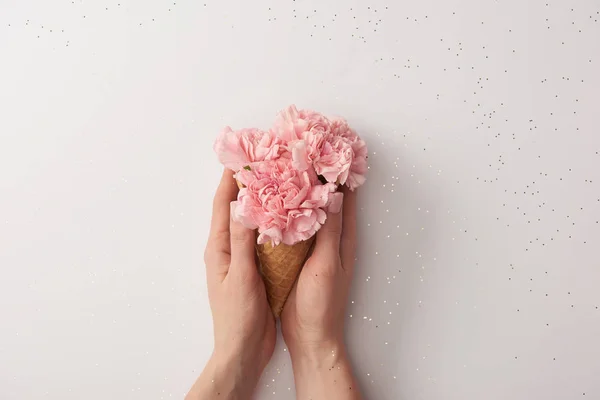 Vista parcial de la mujer sosteniendo cono de gofre con hermosas flores rosadas aisladas en gris - foto de stock