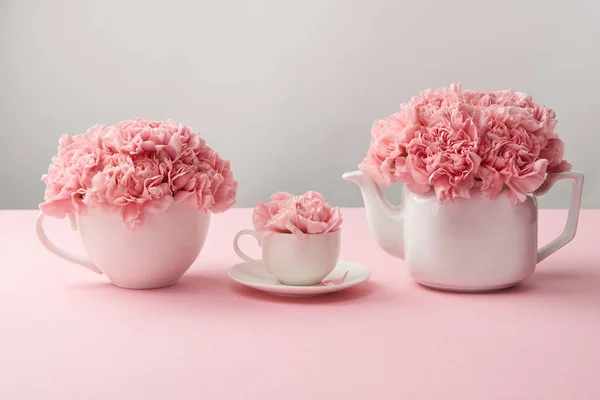 Tazas blancas y hervidor de agua con hermosas flores rosadas en gris — Stock Photo