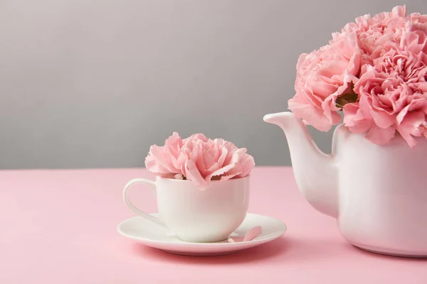 Close-up view of beautiful tender pink flowers in white teapot and cup on grey — Stock Photo