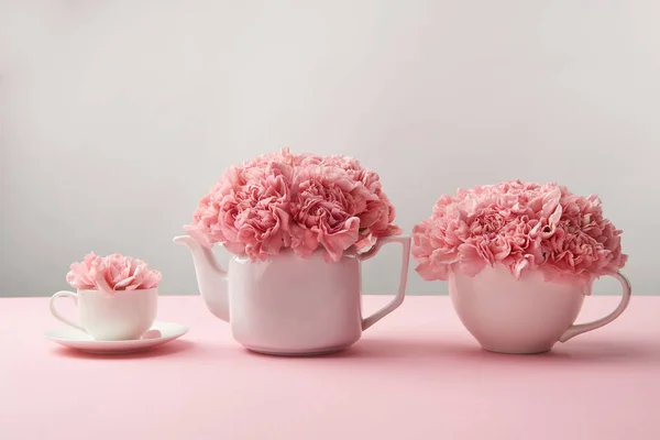 Hermosas flores rosadas tiernas en tetera blanca y tazas en gris - foto de stock