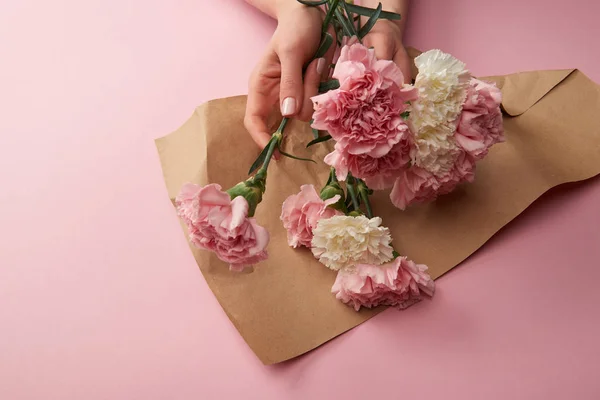 Recortado tiro de mujer envolviendo hermosas flores en papel artesanal en rosa - foto de stock