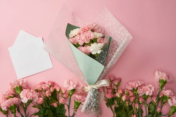 Top view of beautiful bouquet, tender pink flowers and white envelope with card isolated on pink — Stock Photo