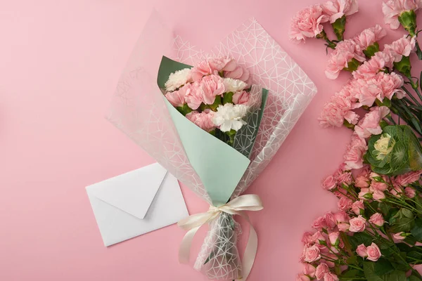 Top view of beautiful tender flower bouquet and white envelope isolated on pink — Stock Photo