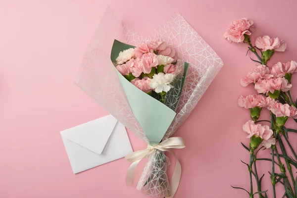 Schöner Strauß, rosa Nelkenblüten und weißer Umschlag isoliert auf rosa — Stockfoto