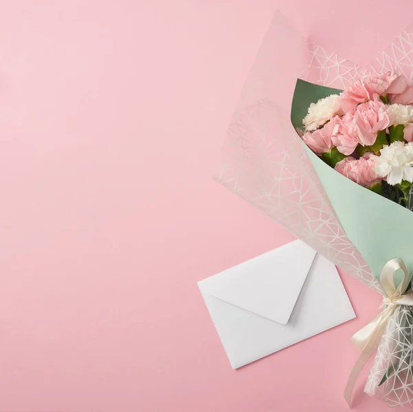 Bellissimo mazzo di fiori teneri e busta bianca isolata su sfondo rosa — Foto stock