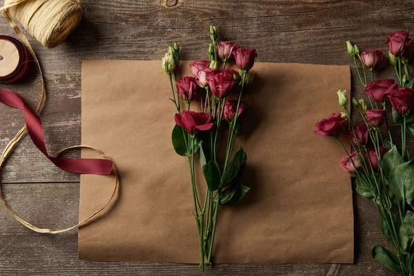 Vista superior de belas flores de eustoma vermelho em papel artesanal e fitas na superfície de madeira — Fotografia de Stock
