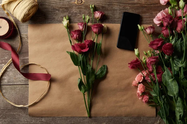 Draufsicht auf schöne Blumen, Smartphone mit leerem Bildschirm, Schere und Schleifen auf Bastelpapier — Stockfoto