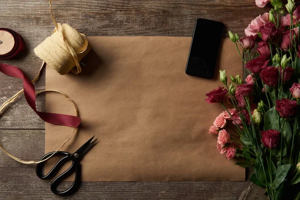 Vista dall'alto di bellissimi fiori vari, smartphone con schermo bianco, forbici e nastri su carta artigianale — Foto stock