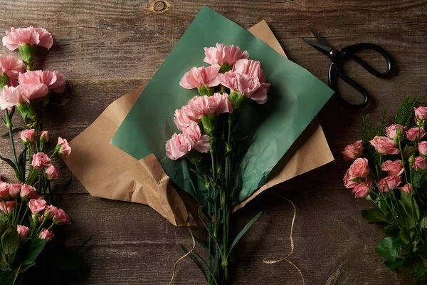 Top view of beautiful pink flowers with craft paper and scissors on wooden surface — Stock Photo