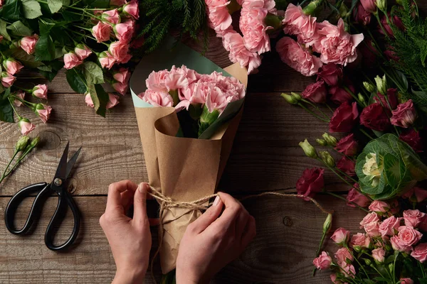 Обрізаний знімок жіночих рук, що друкують мотузку на красивому букеті і ніжні квіти з ножицями на дерев'яній поверхні — стокове фото