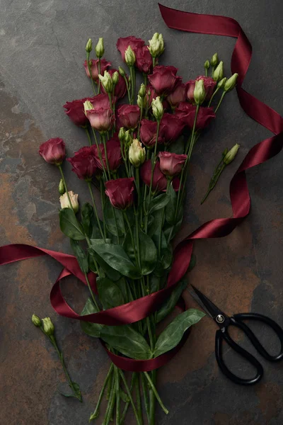 Top view of beautiful red eustoma flowers and scissors on dark surface — Stock Photo