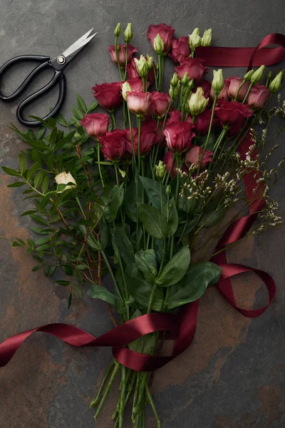 Belas flores de eustoma vermelho com fita e tesoura na superfície escura — Fotografia de Stock