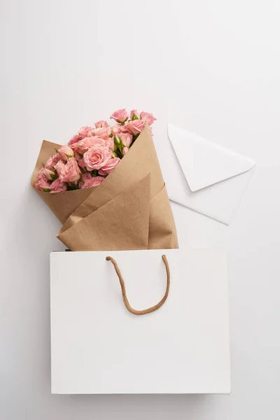 Buquê de belas rosas rosa e envelope branco em saco de papel em cinza — Fotografia de Stock