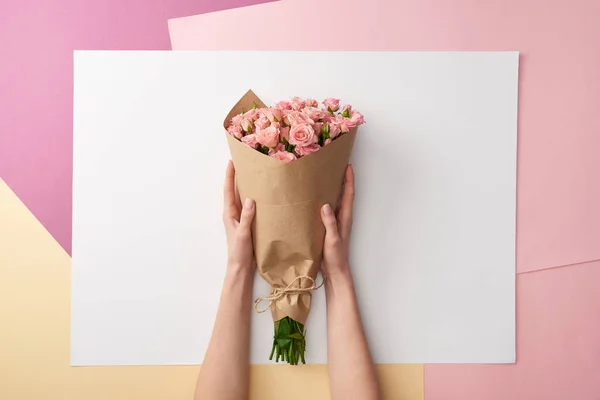 Cropped shot of female hands holding bouquet of beautiful pink roses wrapped in craft paper — Stock Photo