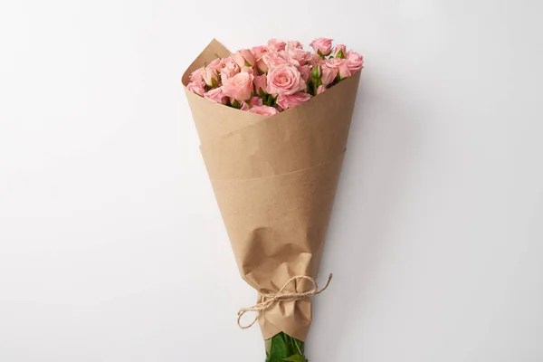 Букет красивих рожевих троянд, загорнутий у ремісничий папір на сірому — стокове фото