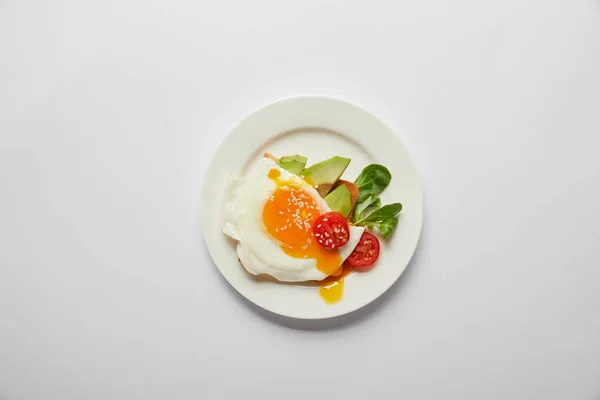 Вид зверху яєчня з вишневим помідором і авокадо в тарілці на сірому фоні — стокове фото
