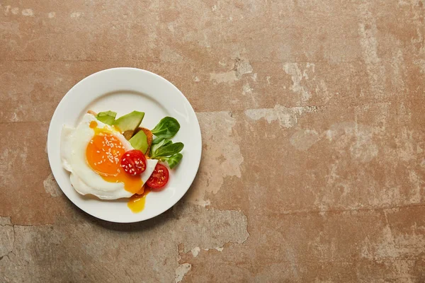 Draufsicht auf Rührei mit Kirschtomaten und Avocado im Teller auf strukturiertem Hintergrund — Stockfoto