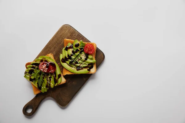 Top view of toasts with avocado and cherry tomato on wooden cutting board on grey background — Stock Photo