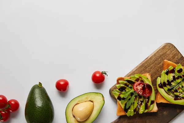 Draufsicht auf Toasts auf Holzschneidebrett mit Avocados und Kirschtomaten auf grauem Hintergrund — Stockfoto