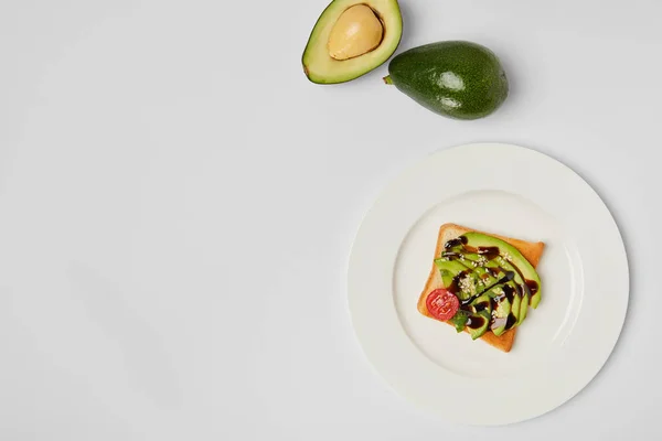 Draufsicht auf Toast mit Avocados und Kirschtomaten auf weißem Teller auf grauem Hintergrund — Stockfoto